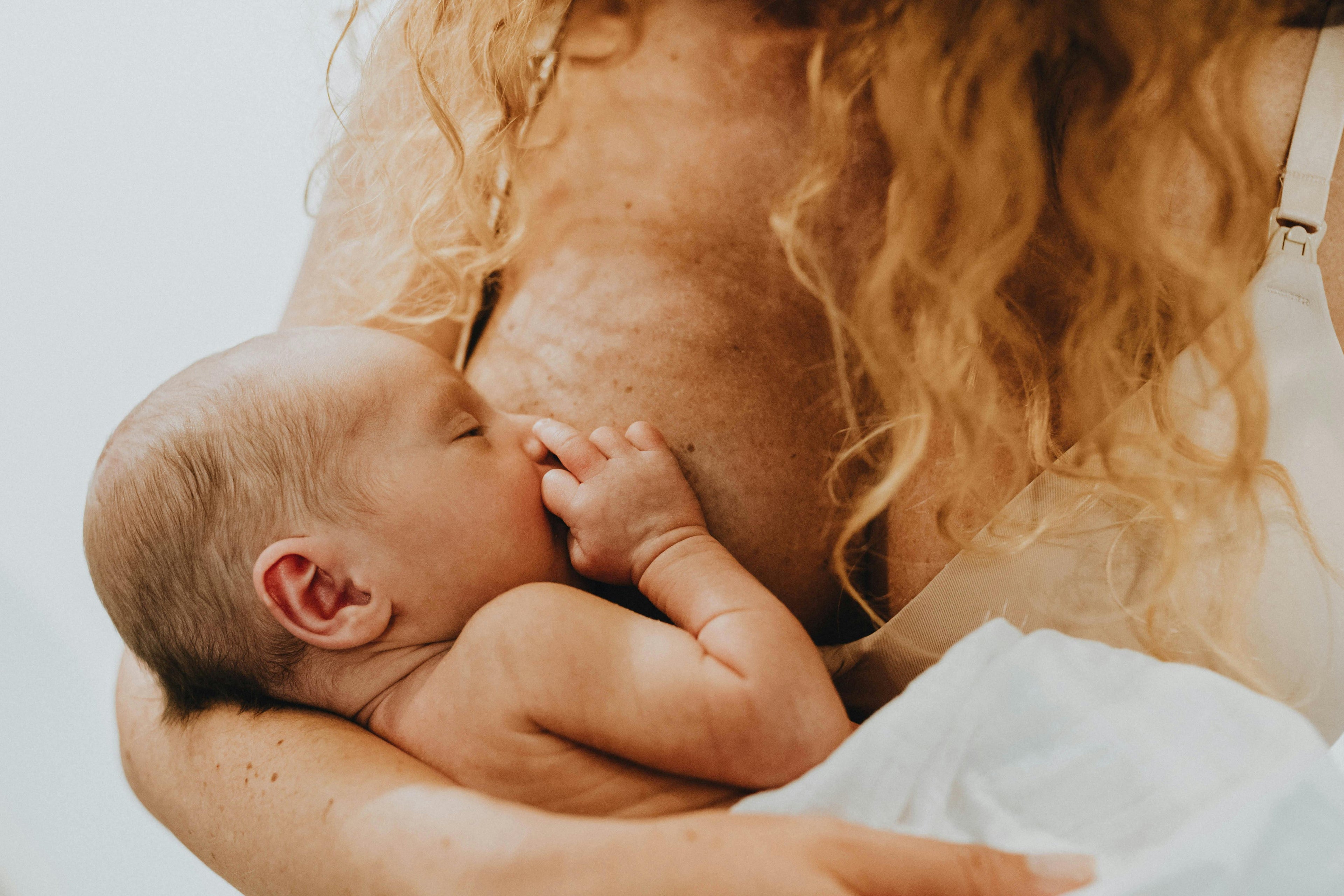 Newborn baby being held by a person with long hair against a neutral background. tta Today Tomorrow & Always   