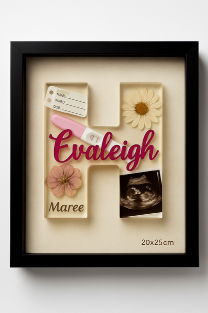 Decorative pregnancy announcement shadow box with 'Evaleigh Maree' and floral elements on a white background. Contains pregnancy test, ultrasound photo